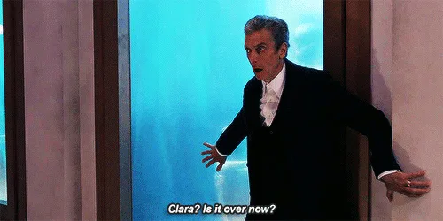 The image shows a man in a black tuxedo with a white shirt and bow tie, standing in a doorway with his hands on the…