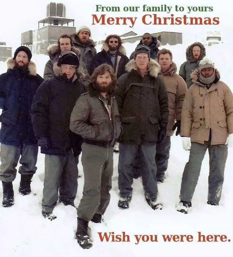 A group of men in heavy winter coats and hats stand in deep snow in front of a building, looking at the camera. The image…