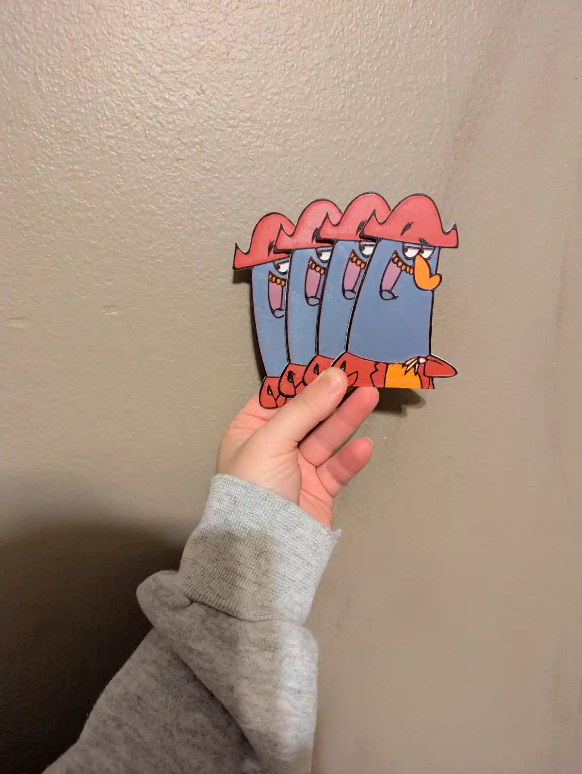 A hand holds up a cutout of the animated character Mr. Krabs from SpongeBob SquarePants, but the cutout is duplicated and…