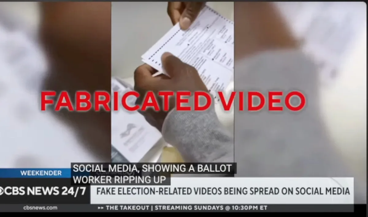 A CBS News 24/7 broadcast graphic overlays a video clip of hands holding a ballot. Large red text reads 'FABRICATED VIDEO'…