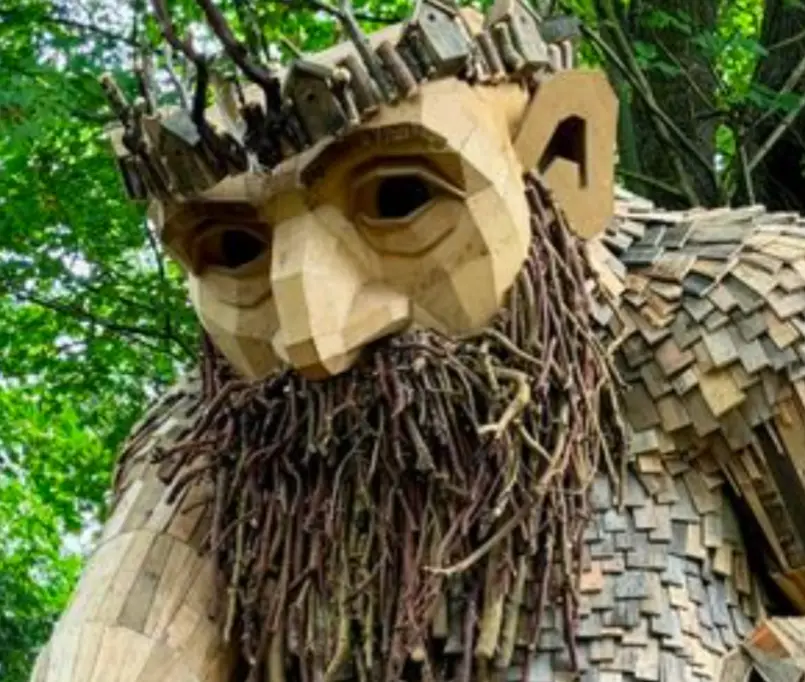 A large, intricately carved wooden sculpture of a bearded man with a crown of branches and twig beard, set against a…