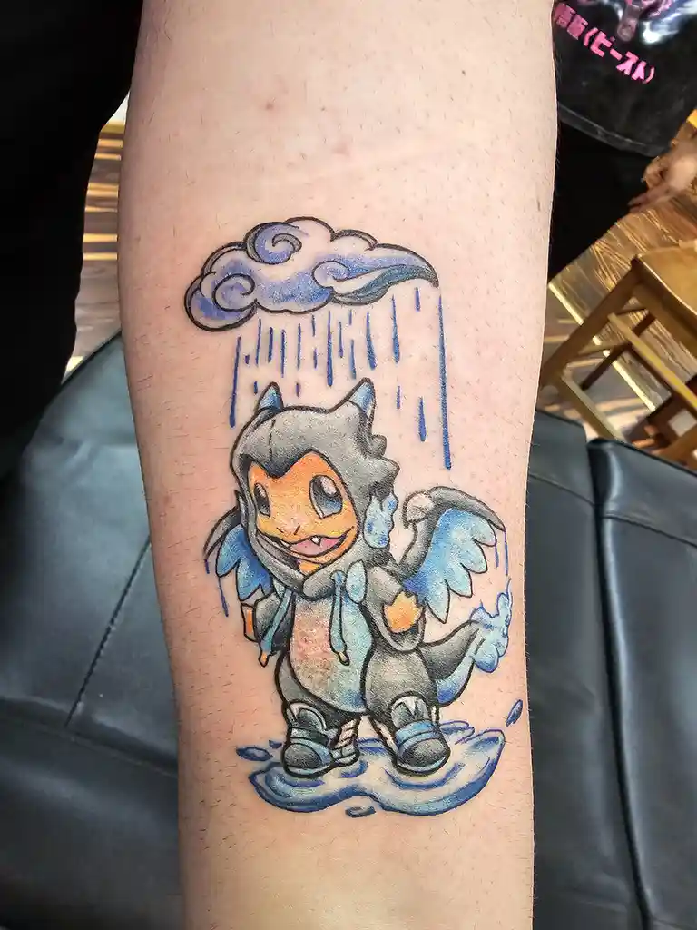 A tattoo on a person's leg depicts a cartoon-style, chibi-style Pokémon character with blue wings and a grey hooded outfit…