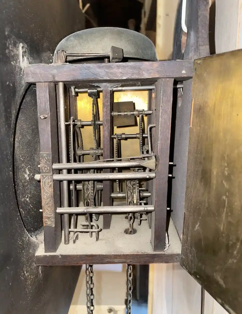 A close-up of an antique clock's internal mechanism, showing exposed gears, chains, and wooden framing. The overlaid text…
