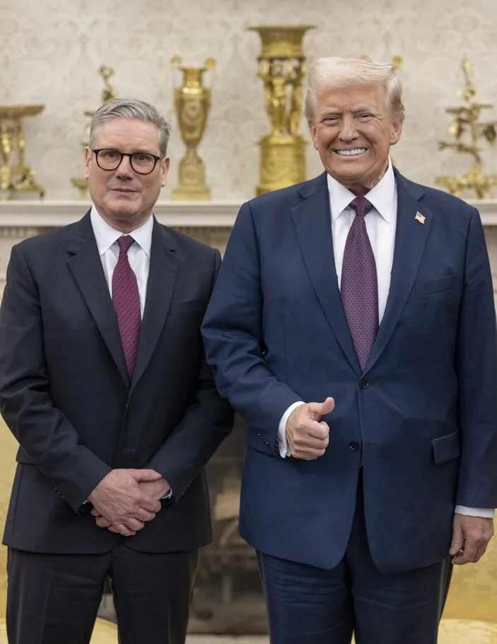 Two men in suits stand side by side in a formal room with ornate golden decor. The man on the right, Donald Trump, smiles…