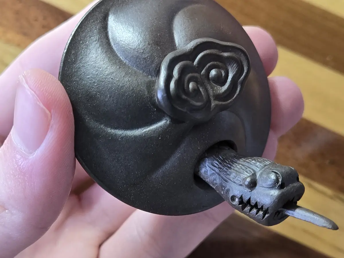 A hand holds a dark, round, metallic object resembling a dragon ball, featuring a carved cloud symbol on top and a dragon's…