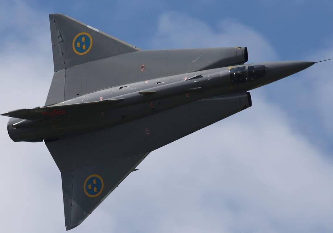 A grey Swedish Saab 37 Viggen fighter jet is captured in flight against a partly cloudy blue sky, viewed from below and…