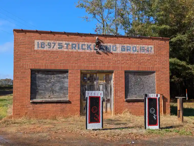 An abandoned brick building with boarded-up windows and a faded sign reading '1897 STRICKLAND GRO. 1947' stands under a…