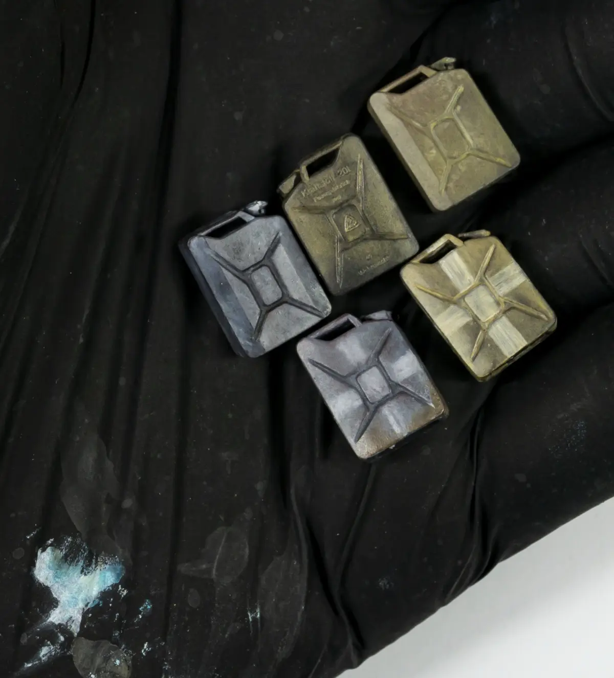 A black-gloved hand holds four small, rectangular metal containers with a distinctive cross-hatched design, resembling…