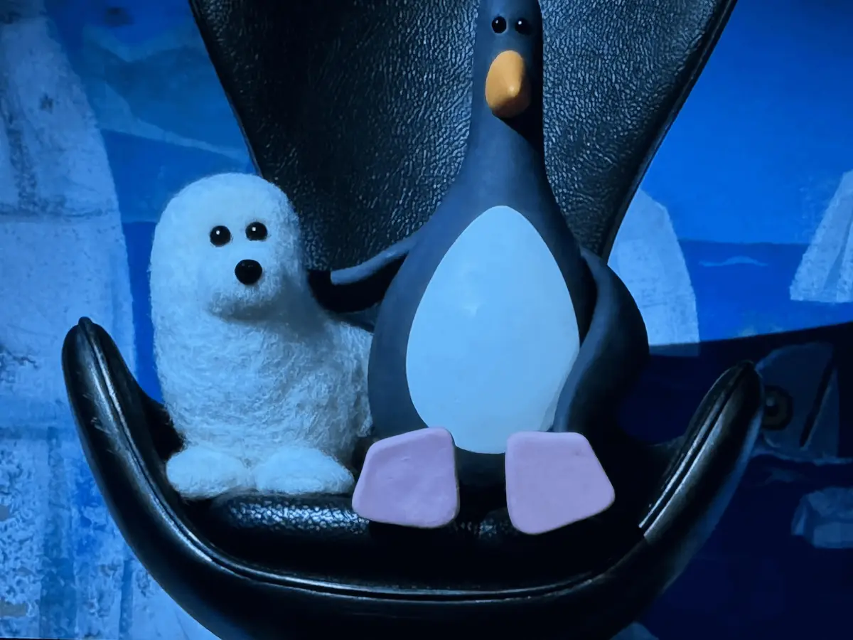 A still from the stop-motion animated film 'Pingu' shows a large penguin character with its wings spread, sitting in a black…