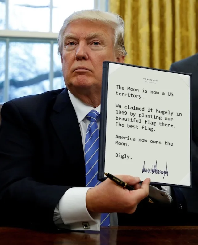A man in a dark suit and blue striped tie sits at a desk holding a framed document that reads 'The Moon is now a US…