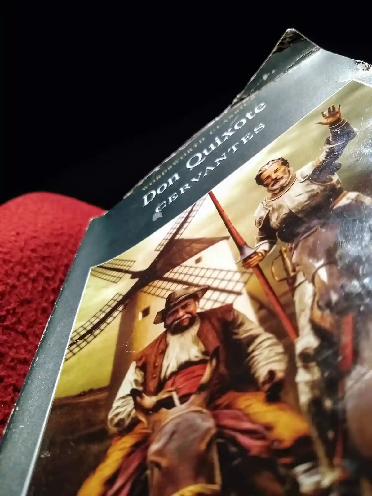 A close-up, angled shot of a worn paperback book cover for 'Don Quixote' by Cervantes, showing the illustrated cover art of…