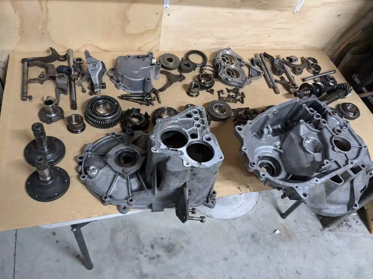A disassembled motorcycle engine with its two main halves and numerous small parts like gears, bearings, bolts, and shafts…