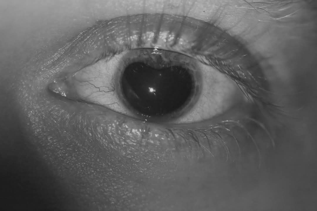 A black-and-white close-up of a human eye with visible tear streaks and a glossy reflection in the pupil. The overlaid text…