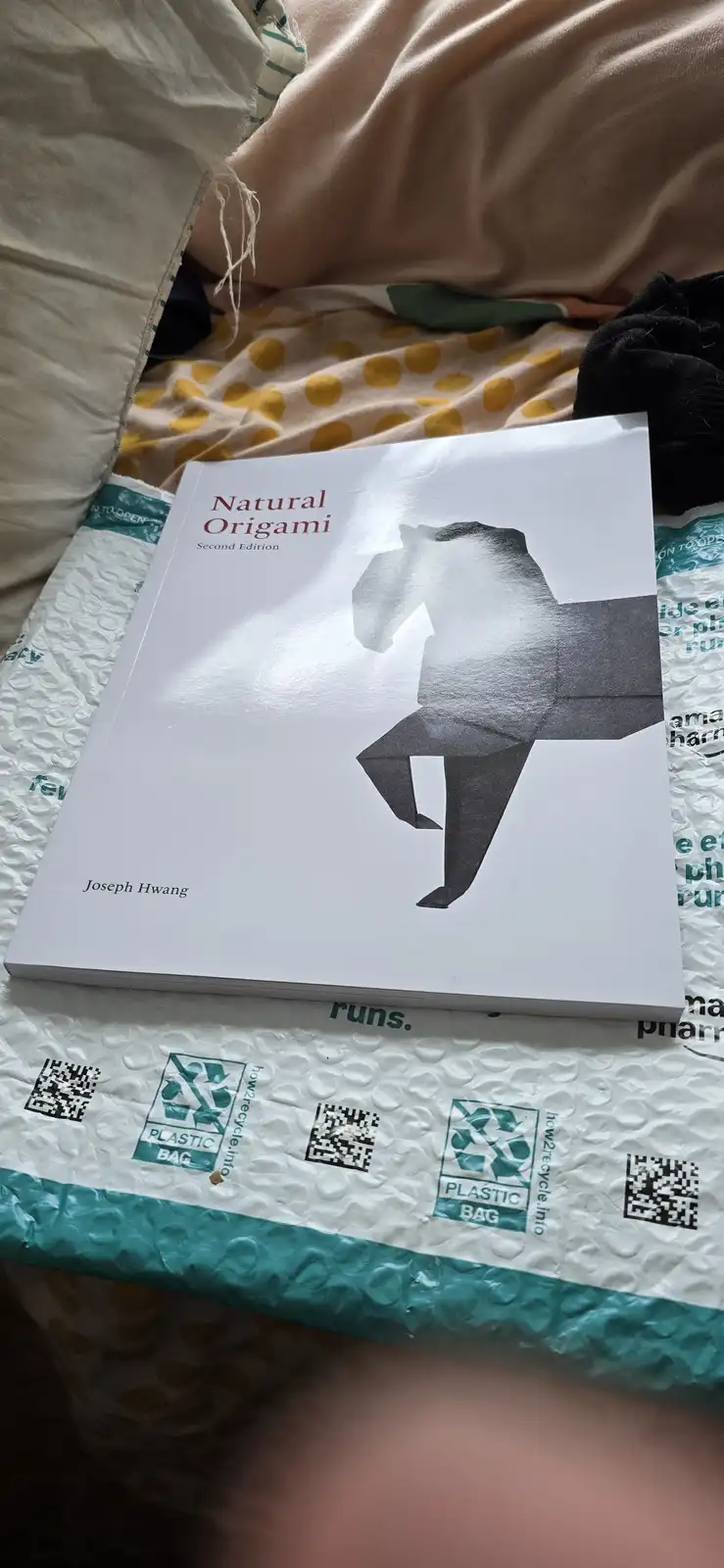 A book titled 'Natural Origami, Second Edition' by Joseph Hwang, featuring a grayscale origami figure on its cover, rests on…