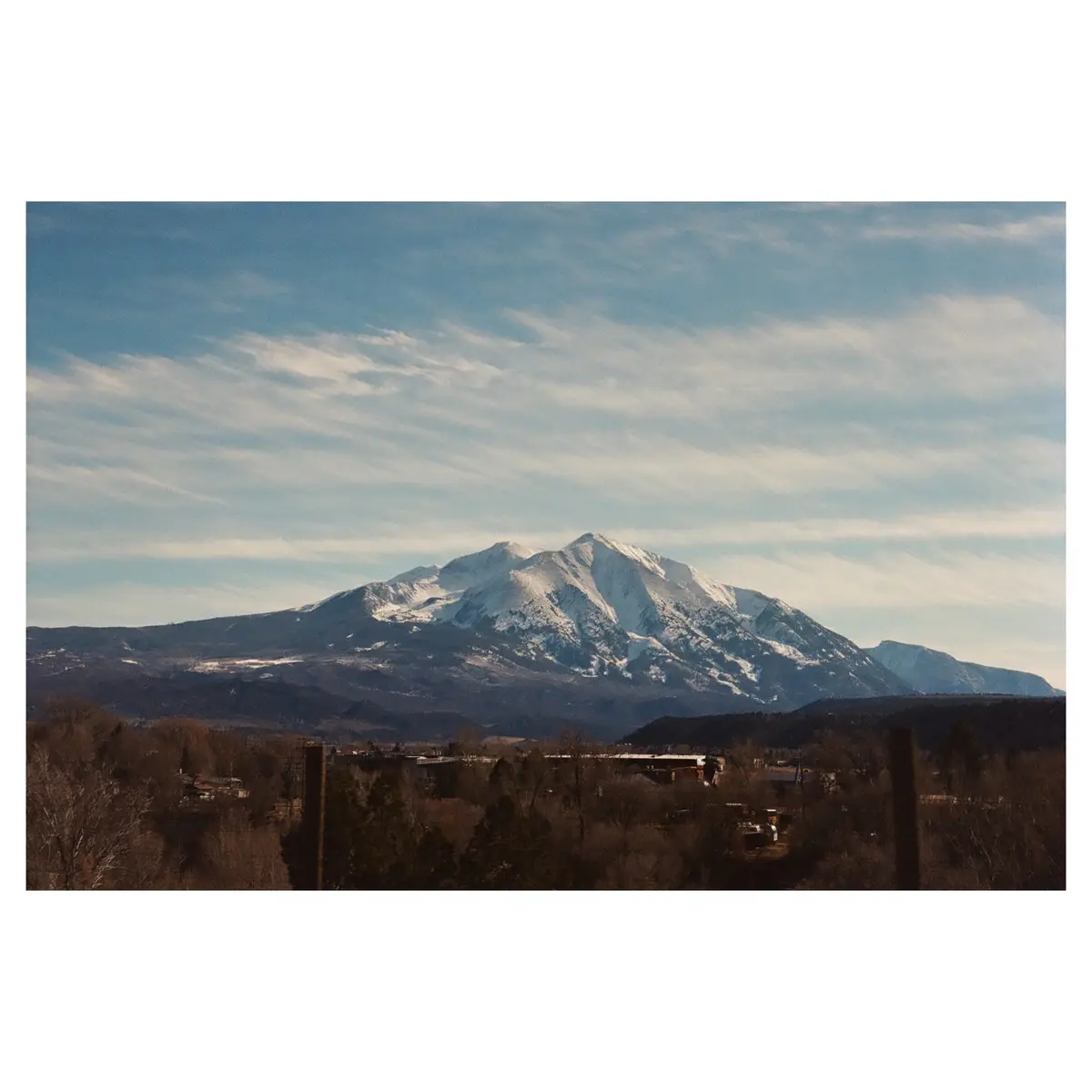 A scenic photograph shows a snow-capped mountain range under a partly cloudy blue sky, with a foreground of bare trees and…