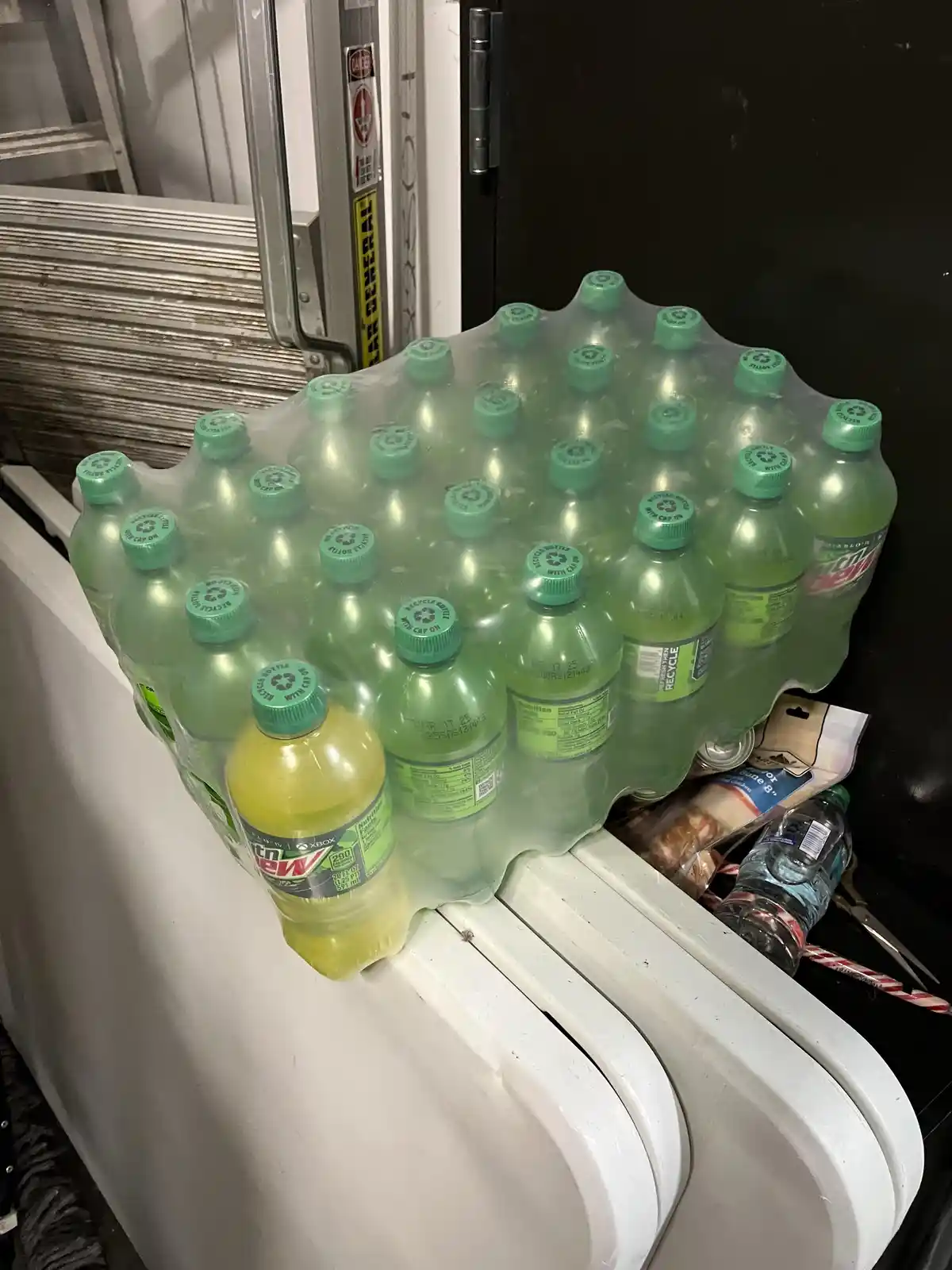A large plastic pack of Mountain Dew soda bottles sits on a white surface, with one bottle in the front having a noticeably…