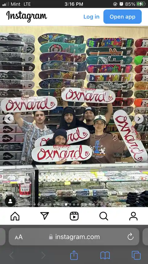 Five men are posing in a skateboard shop, each holding up a white skateboard deck with the word 'Oxnard' written in red…