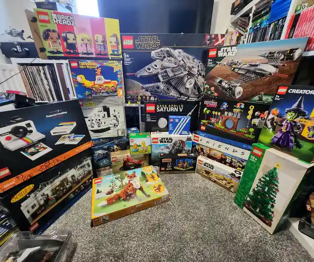 A floor is covered with numerous LEGO set boxes, including Star Wars, Friends, The Beatles, Seinfeld, Sonic the Hedgehog…