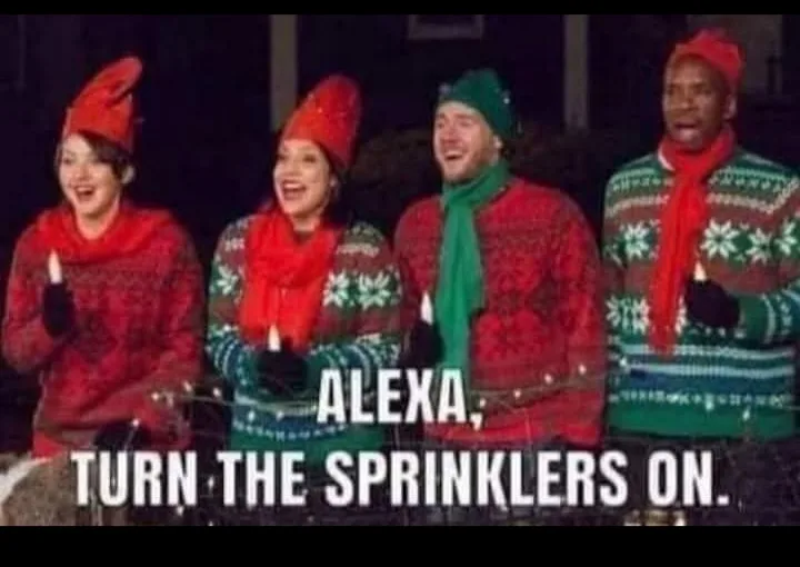Four people dressed in festive holiday sweaters and hats stand in a line, holding candles, with a dark background. The…