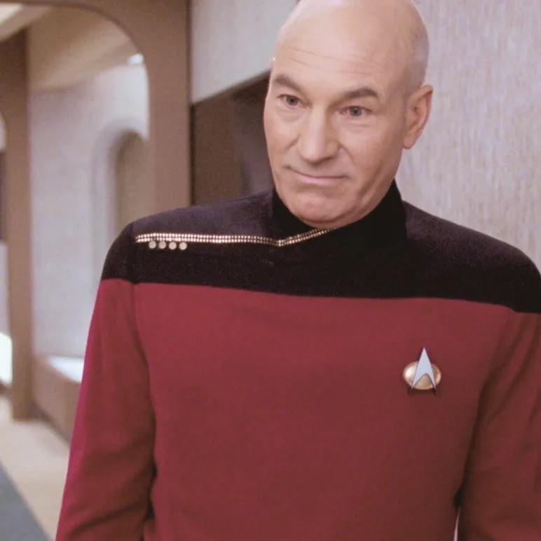 A man in a red and black Starfleet uniform with a captain's insignia looks at the camera with a skeptical, slightly annoyed…