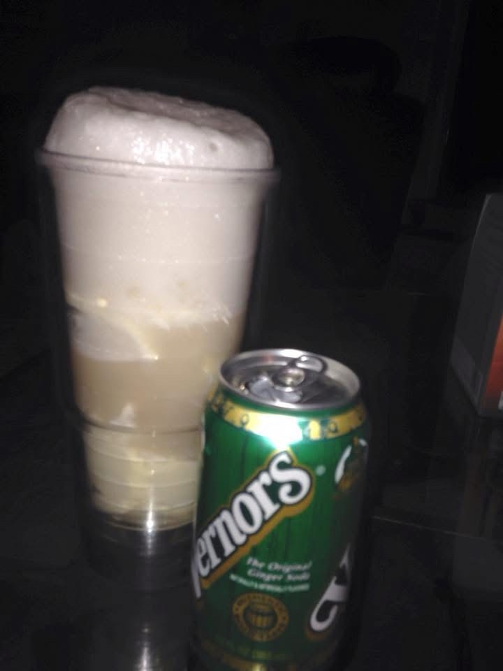 A green can of Pernors ginger soda sits next to a tall glass filled with a foamy, light-colored beverage. The image is dimly…