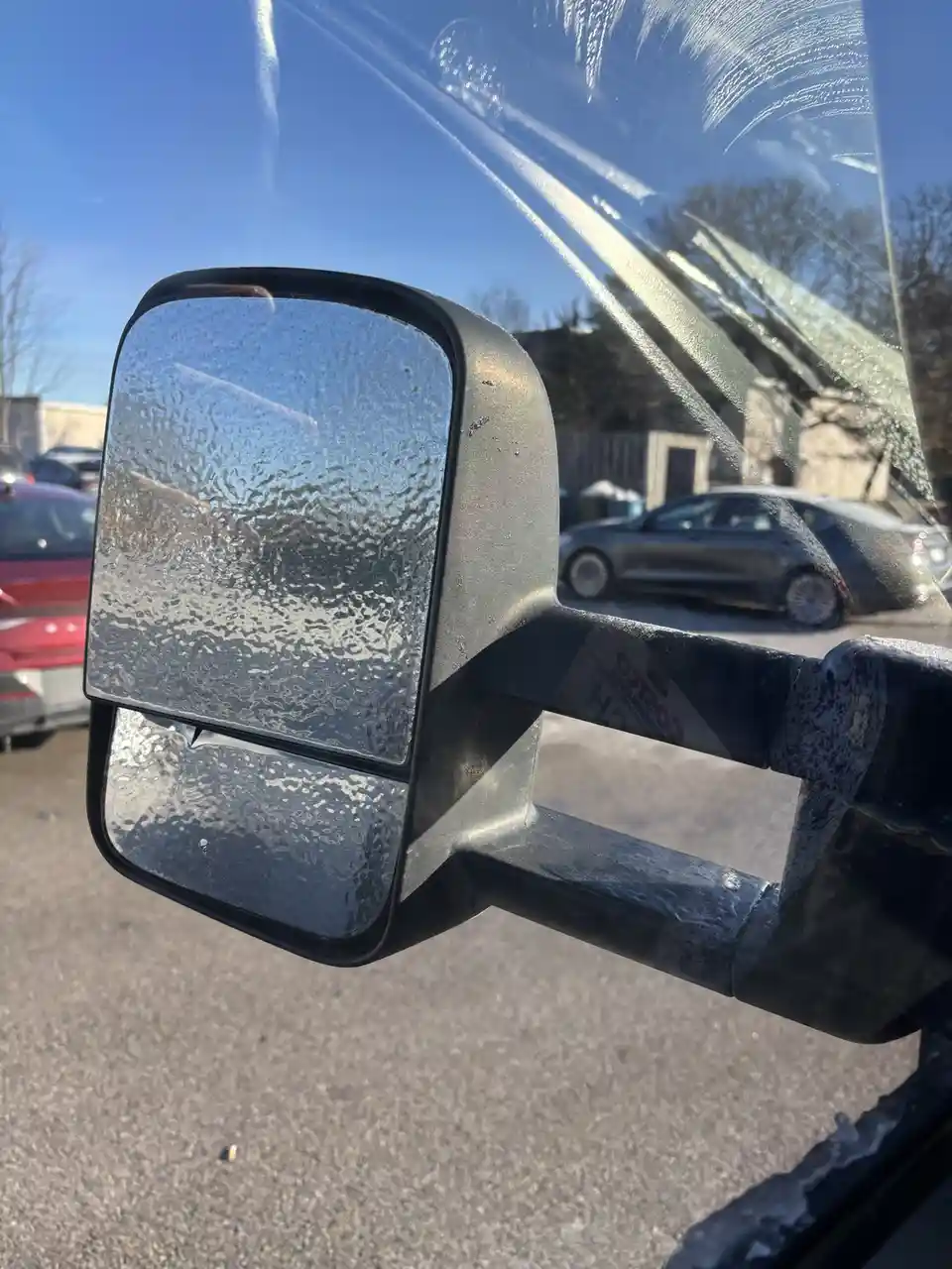 A close-up photo shows a car's side mirror and windshield covered in soap suds and water from a recent wash, with a Costco…