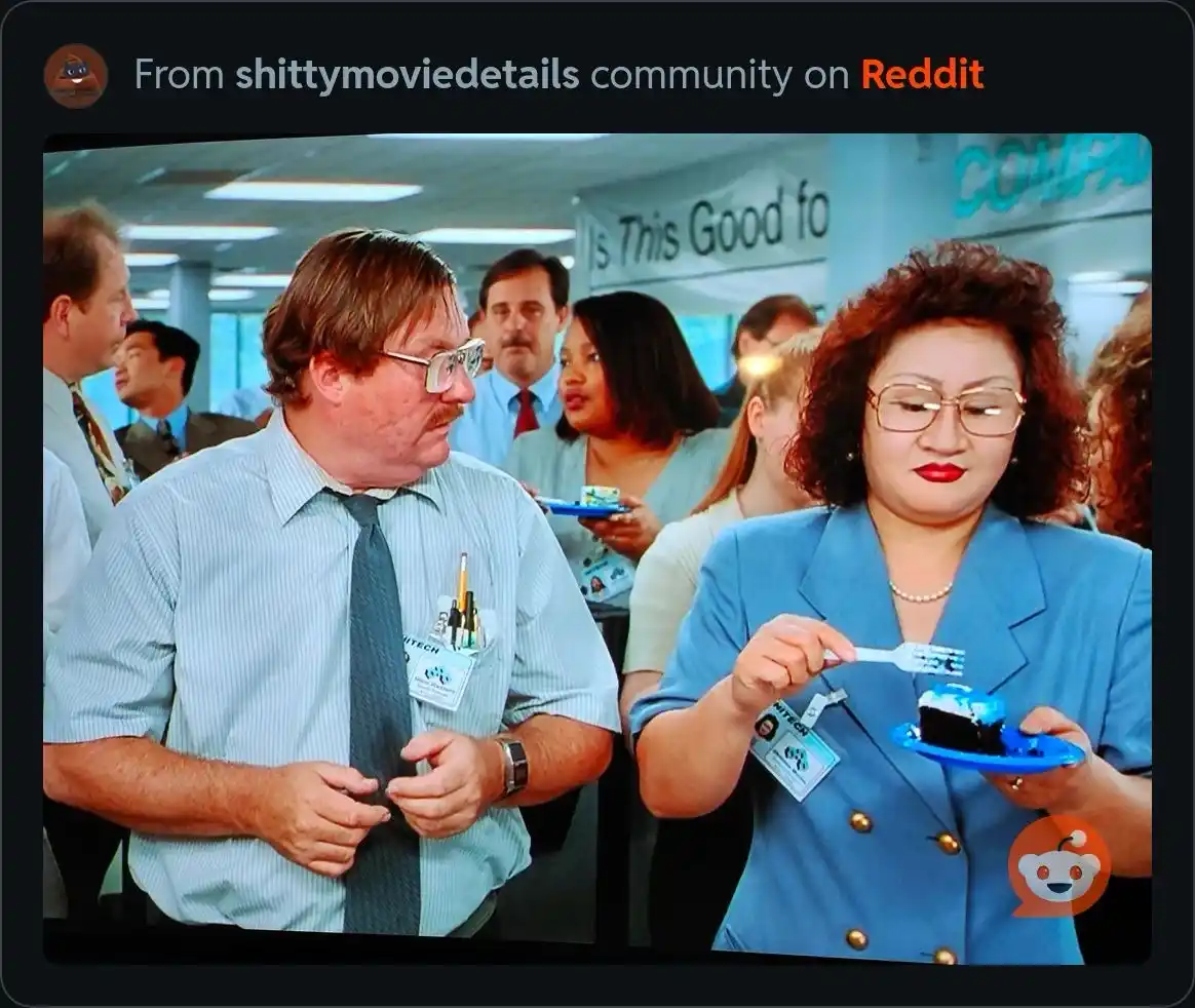 A man in a light blue shirt and tie stands beside a woman in a blue blazer who is eating a piece of cake with a plastic…