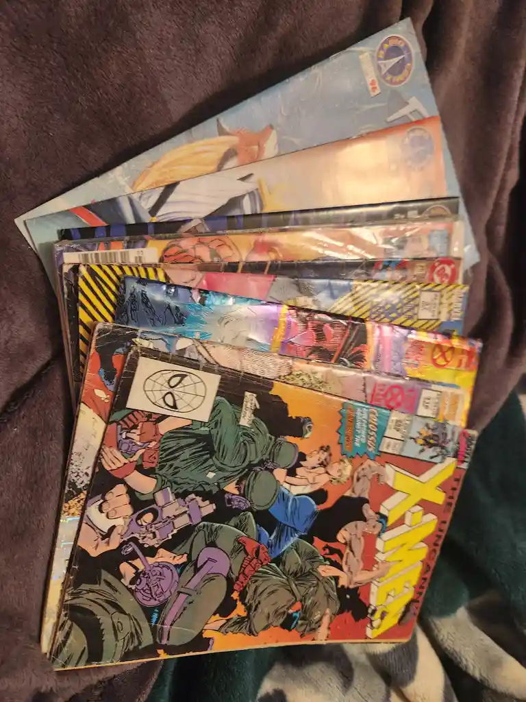 A stack of worn, colorful comic books, including 'The Uncanny X-Men' and others with visible Marvel and DC logos, rests on a…