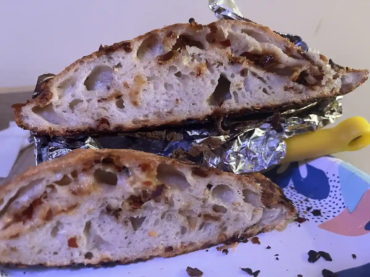 A close-up photo shows two halves of a baked bread roll, cut open to reveal a chewy interior with visible chunks of what…