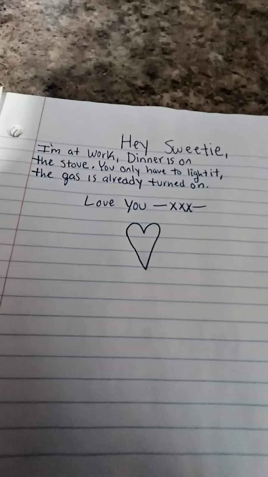 A handwritten note on lined notebook paper rests on a speckled countertop. The note, written in black ink, reads: 'Hey…