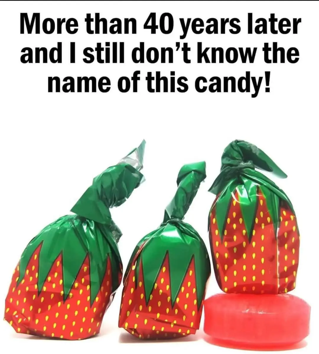 Three strawberry-shaped candies wrapped in red foil with green leaf tops and yellow seeds are shown against a white…