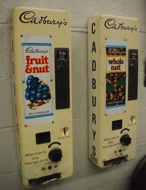 Two vintage Cadbury's chocolate vending machines side by side, one labeled 'fruit & nut' with a blue grape graphic and the…