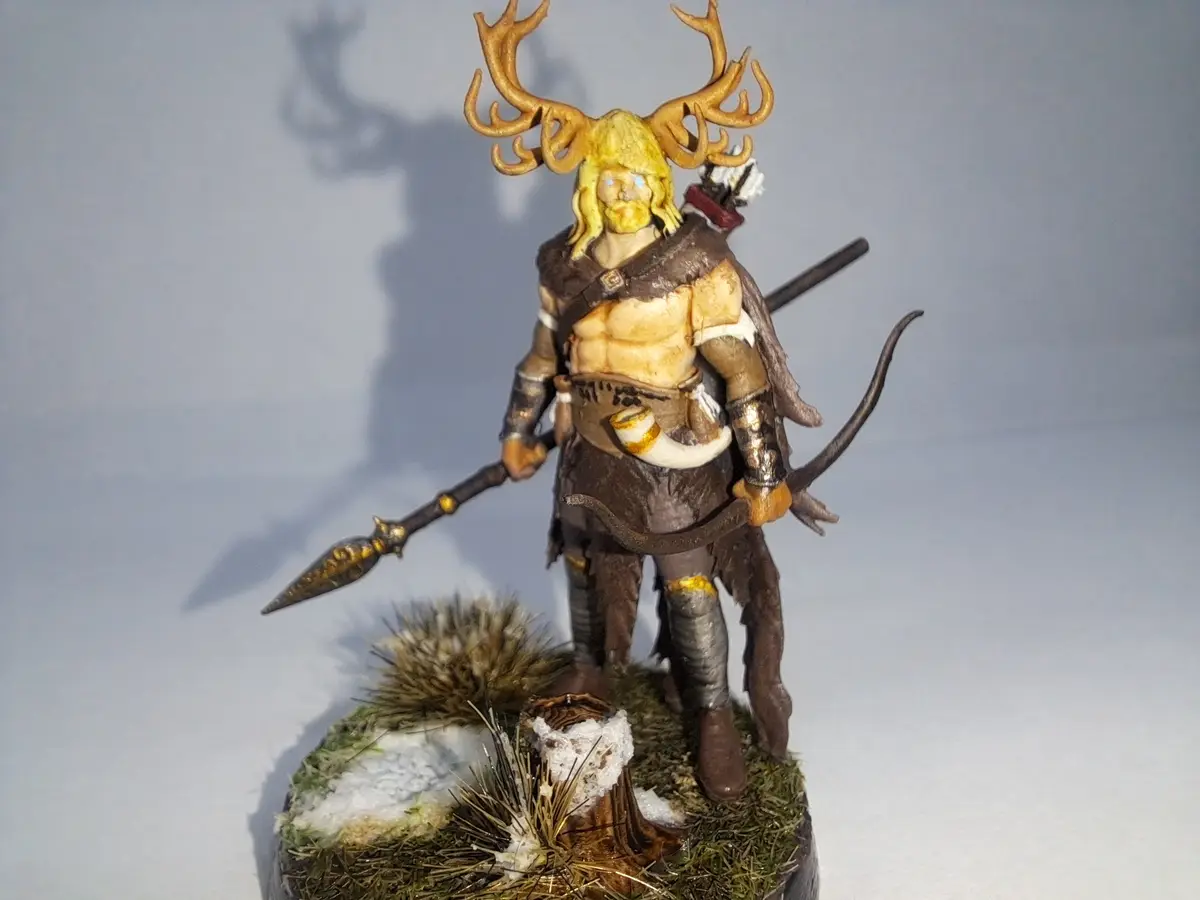 A detailed fantasy miniature of a muscular warrior with large golden antlers, holding a spear and bow, standing on a snowy…