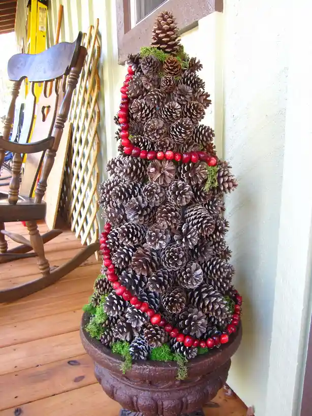 A decorative Christmas tree made entirely of pinecones, adorned with red cranberries and green moss, sits in a dark brown…