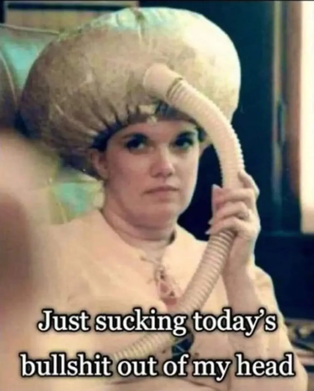 A woman with a vintage hair dryer hood on her head, holding the hose, looks intensely at the camera. The overlaid text reads…