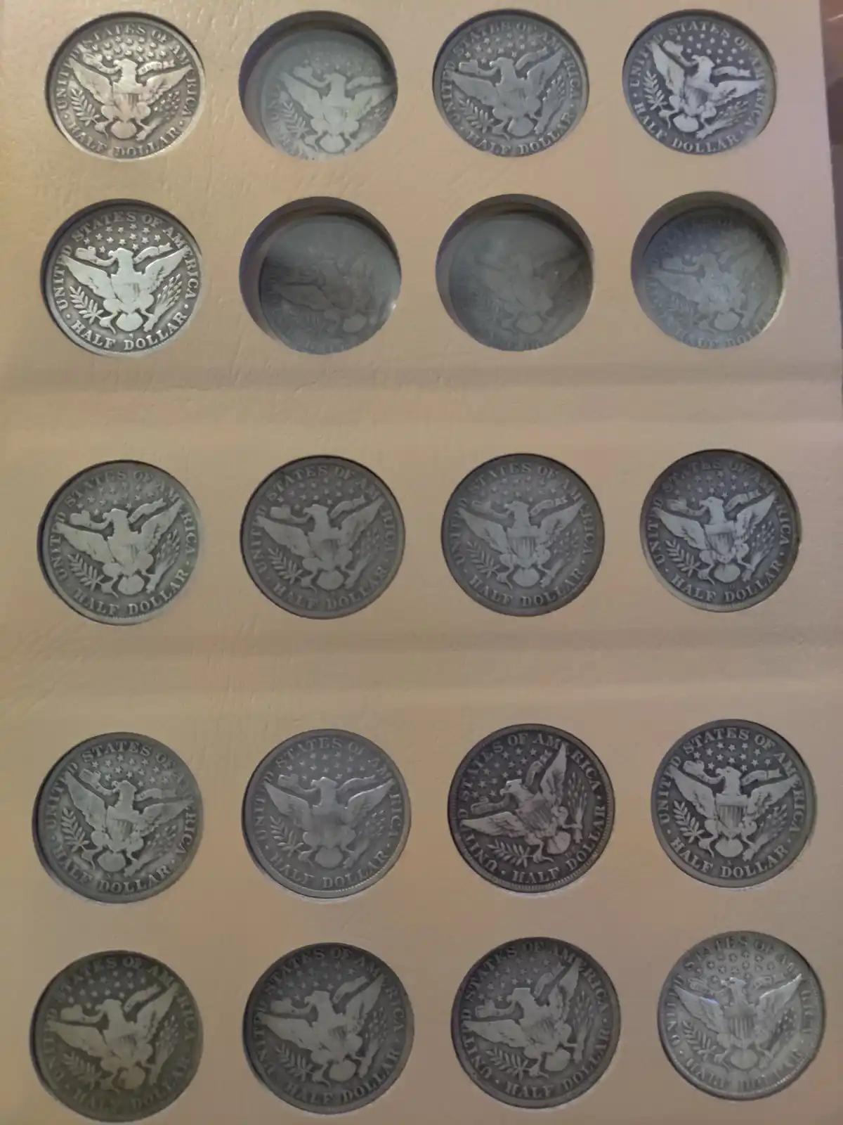 A collection of 20 silver-colored U.S. half dollar coins arranged in a five-by-four grid within a tan-colored coin album…