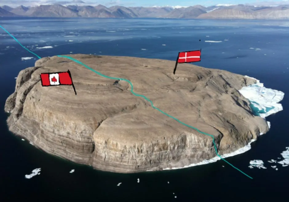 An aerial photo of a small, rocky island surrounded by water and ice, with a Canadian flag and a Danish flag planted on…