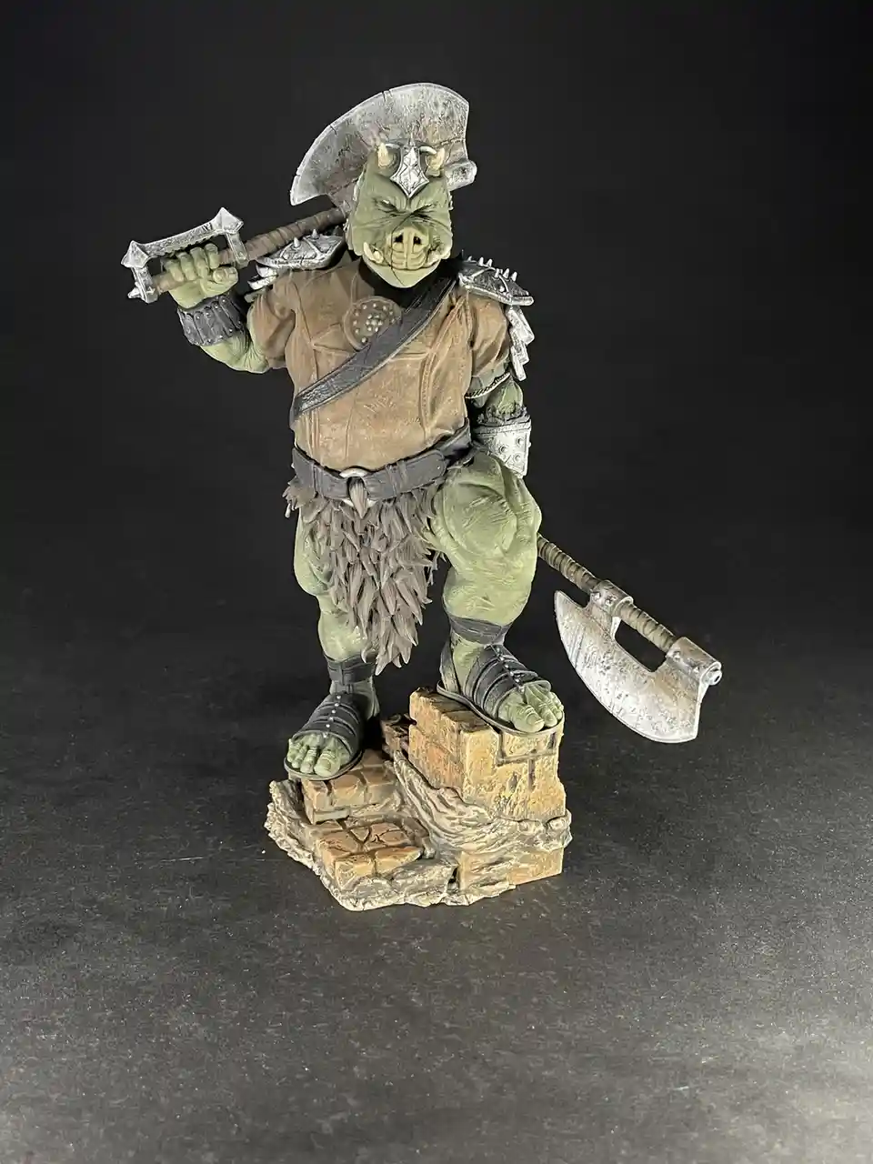 A green-skinned, pig-like fantasy warrior figurine stands on a stone base, wearing armor and holding a large axe over his…