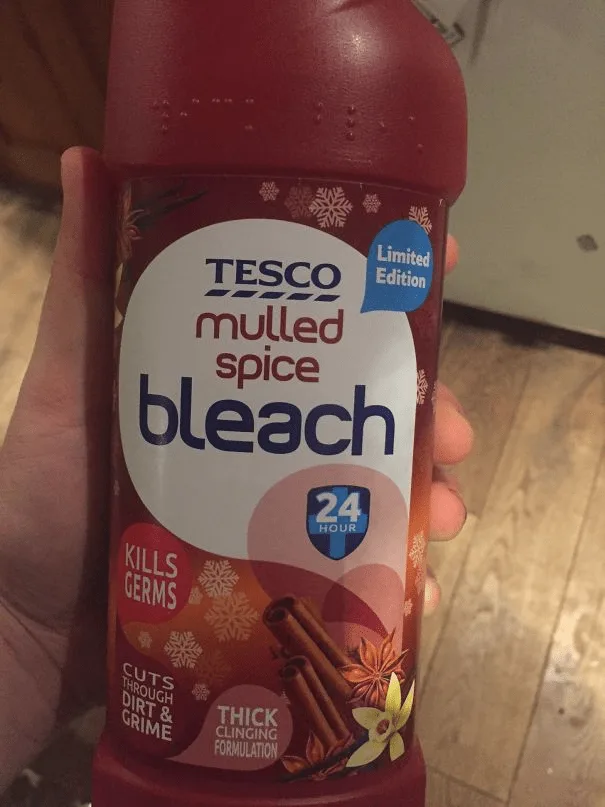 A hand holds a red bottle of Tesco brand bleach labeled 'mulled spice' with festive snowflake graphics, implying a…