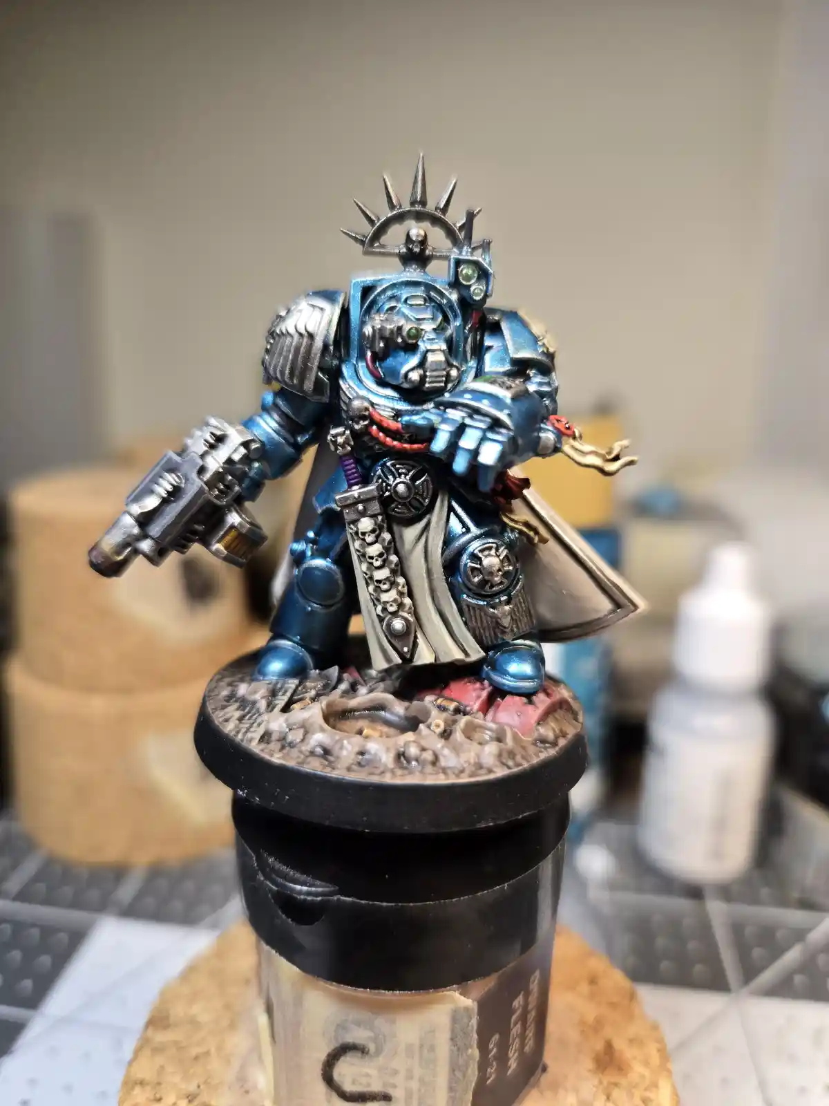 A highly detailed, blue-painted miniature of a Space Marine from Warhammer 40,000 stands on a custom base, holding a weapon…
