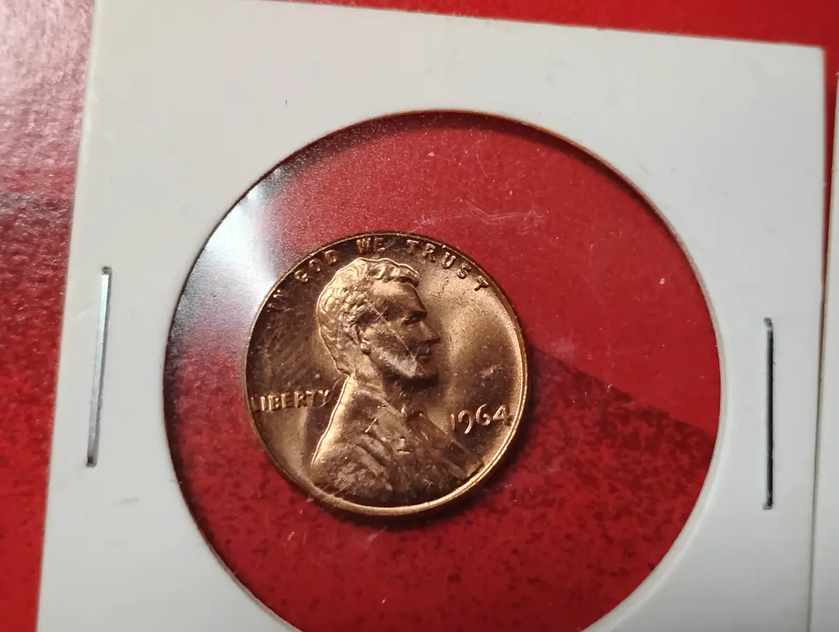 A close-up photo shows a 1964 U.S. Lincoln penny, featuring Abraham Lincoln's profile, encased in a white plastic coin…