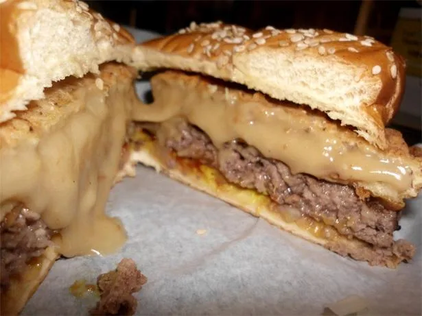 A close-up photo of a cheeseburger that has been sliced in half, revealing a thick beef patty and abundant melted cheese…