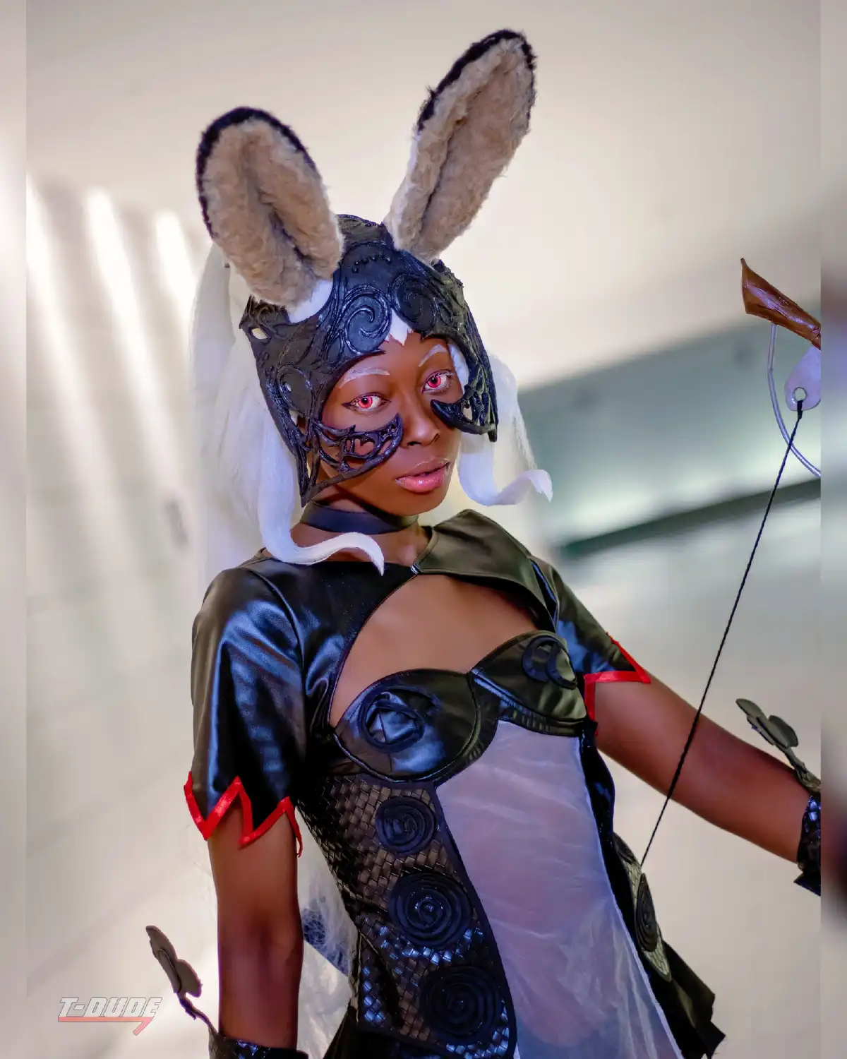 A person in a detailed cosplay costume featuring large, fluffy bunny ears, a black ornate helmet with eye slits, and a black…