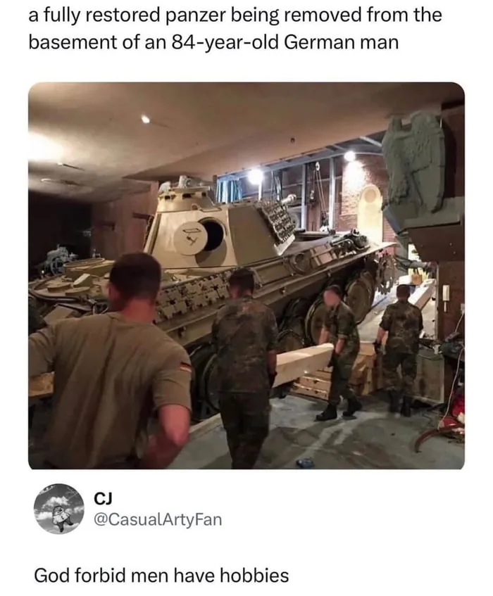 A large, fully restored German Panzer tank is being carefully lifted and moved by several men in military-style clothing…