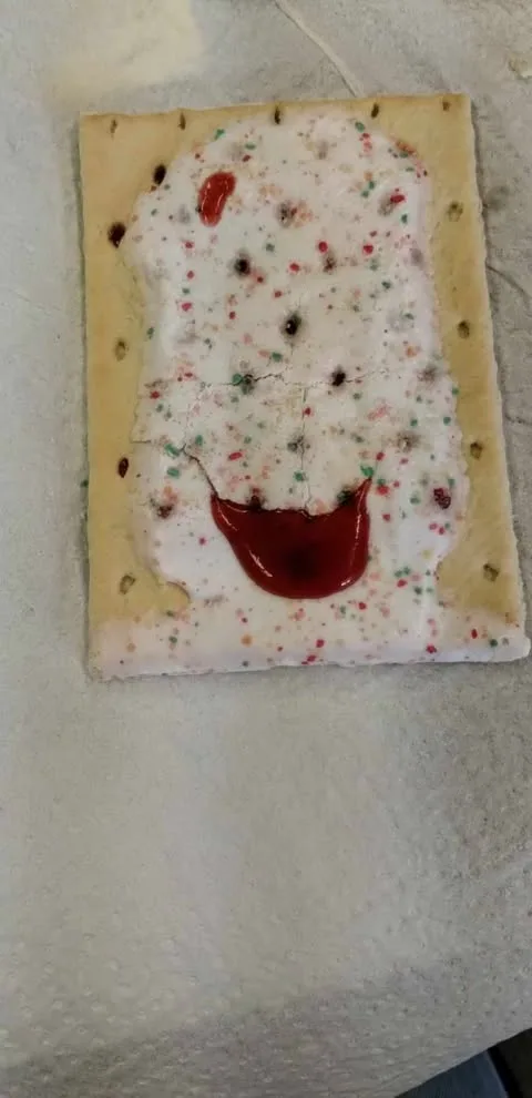 A rectangular, light-brown cracker with white frosting and colorful sprinkles is laid on a paper towel. The frosting has…