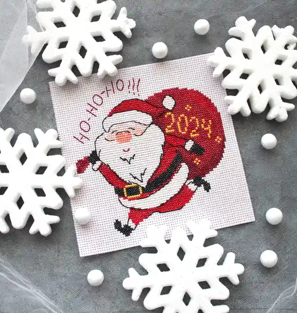 A cross-stitch pattern of a smiling Santa Claus holding a red sack labeled '2024' is surrounded by white snowflake…
