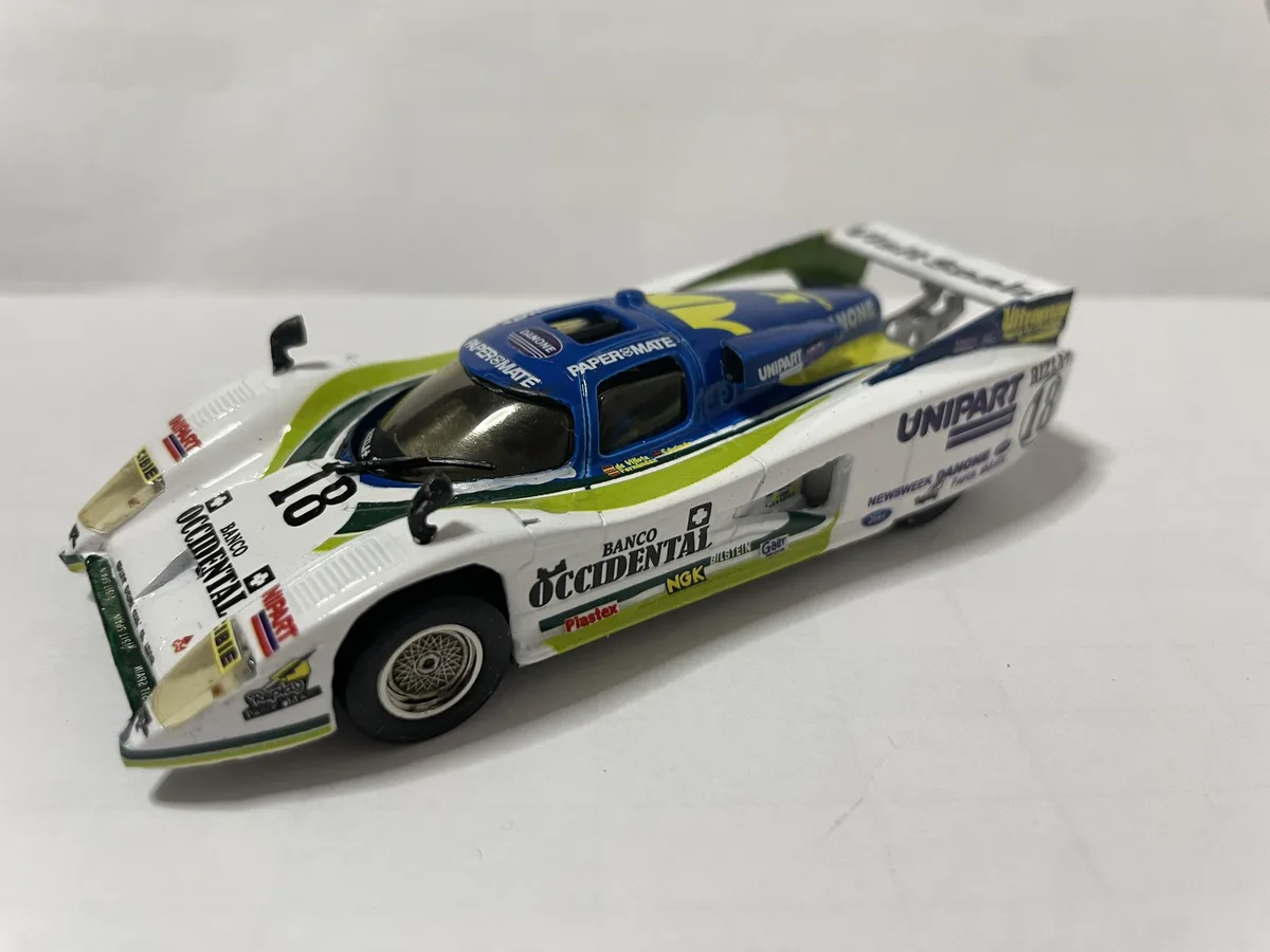 A detailed die-cast model of a white, blue, and green racing car with the number 18, featuring sponsor logos like Unipart…