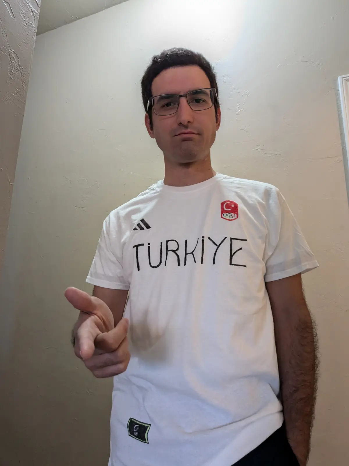 A man wearing a white Turkey Olympic jersey with 'TURKIYE' written across the chest points directly at the camera with a…