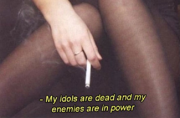 A close-up image shows a person's hand holding a lit cigarette while seated, with visible smoke rising. The person is…