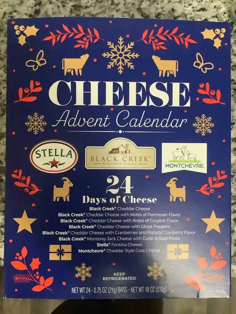 A blue cheese advent calendar box decorated with red holly, gold snowflakes, and goat/cow silhouettes, listing 24 different…
